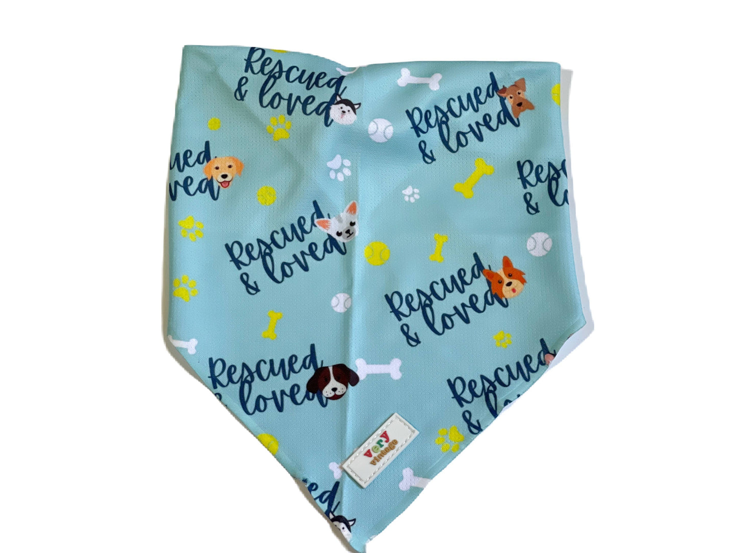 A light blue triangular pet bandana featuring a playful pattern of 'Rescued & loved' text, dog illustrations, bones, and paw prints, with a small white brand tag near the bottom.